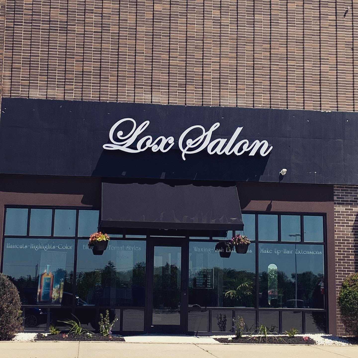 Front view of Lox Salon with glass doors, potted plants, and a large sign above the entrance.