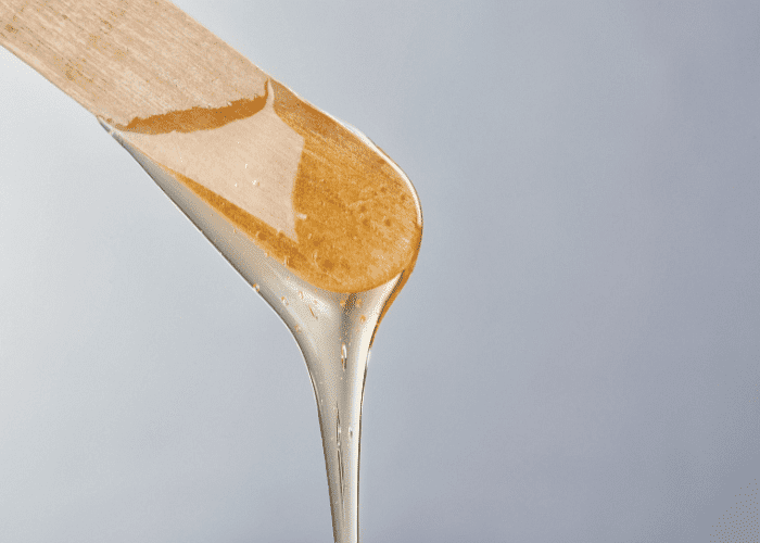 A wooden spatula covered in thick, amber-colored honey against a grey background.