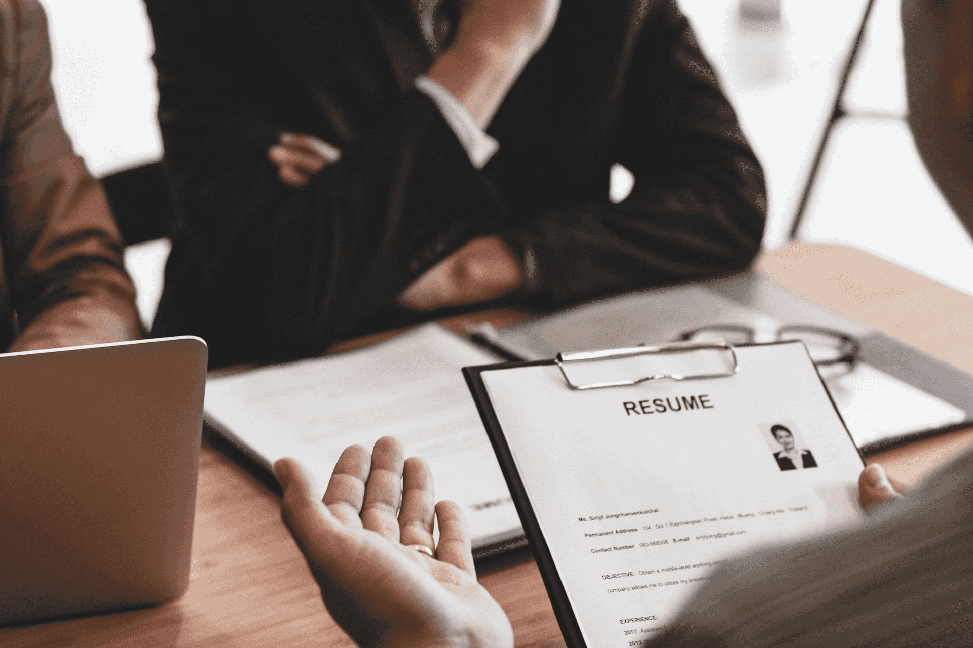 Person holding a resume during an office interview with two employers sitting across the table.