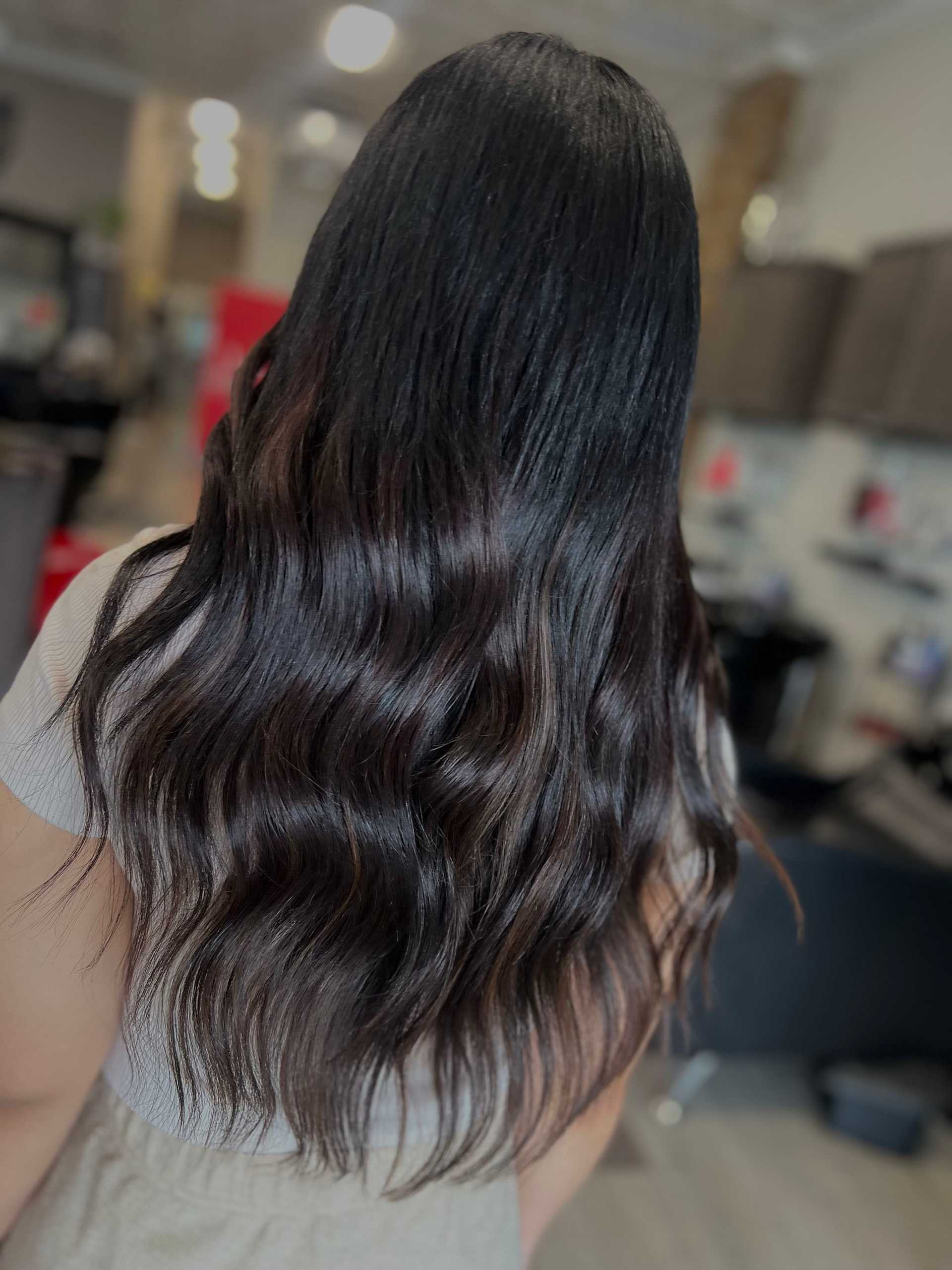 Woman with long, wavy, dark hair inside a modern salon.