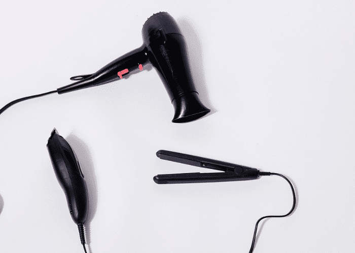 Black hair dryer, hair clipper, and flat iron on a white surface.