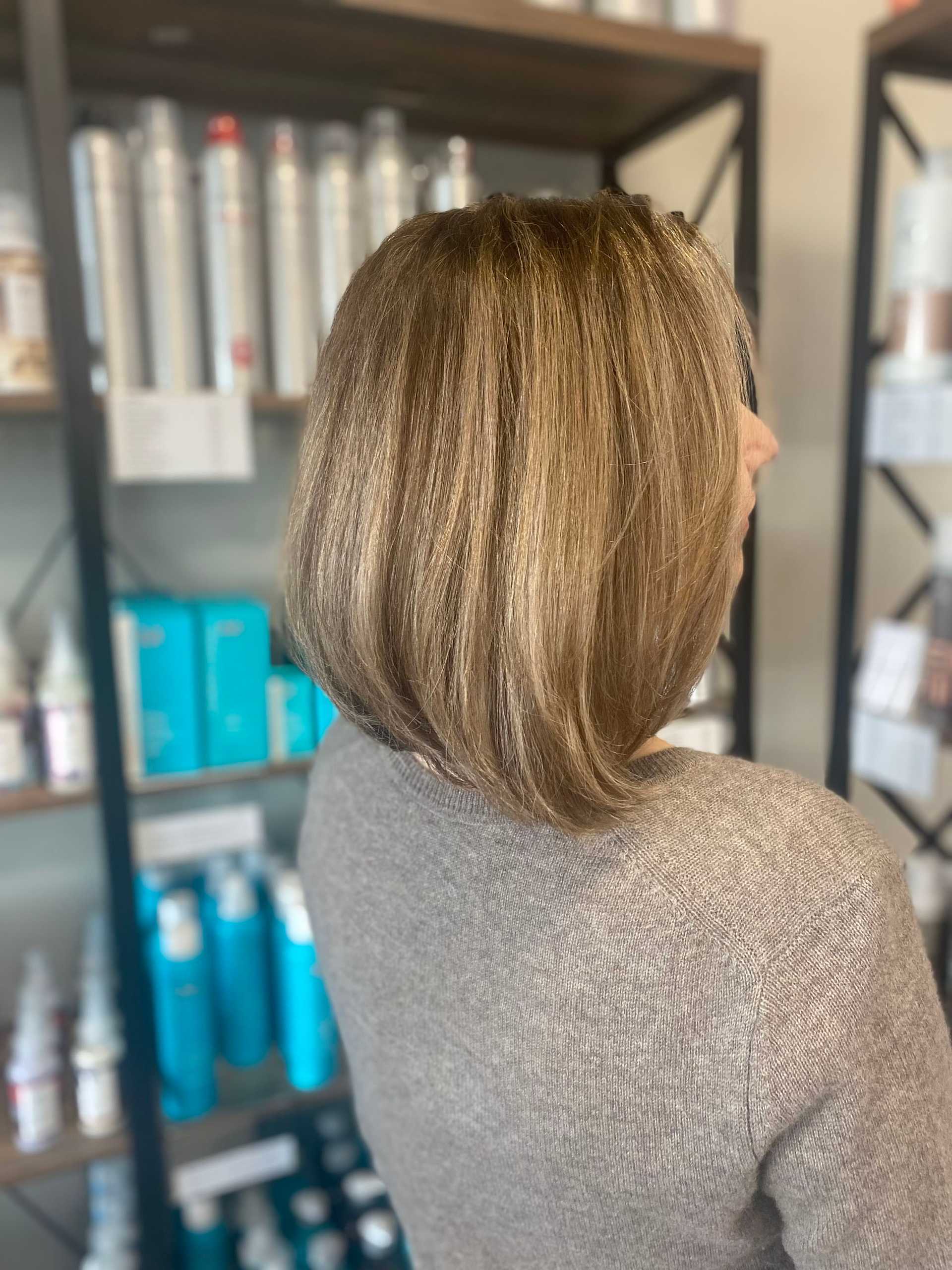 Woman with a stylish bob haircut standing in front of hair products displayed on salon shelves.