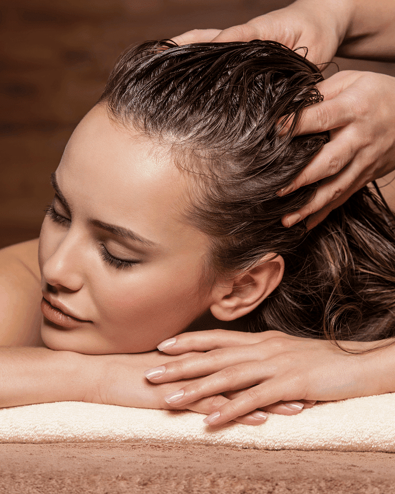 Woman receiving a relaxing head massage with her eyes closed and hands folded on a towel.
