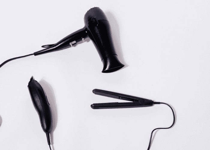 Black hair dryer, hair clipper, and flat iron on a white surface.