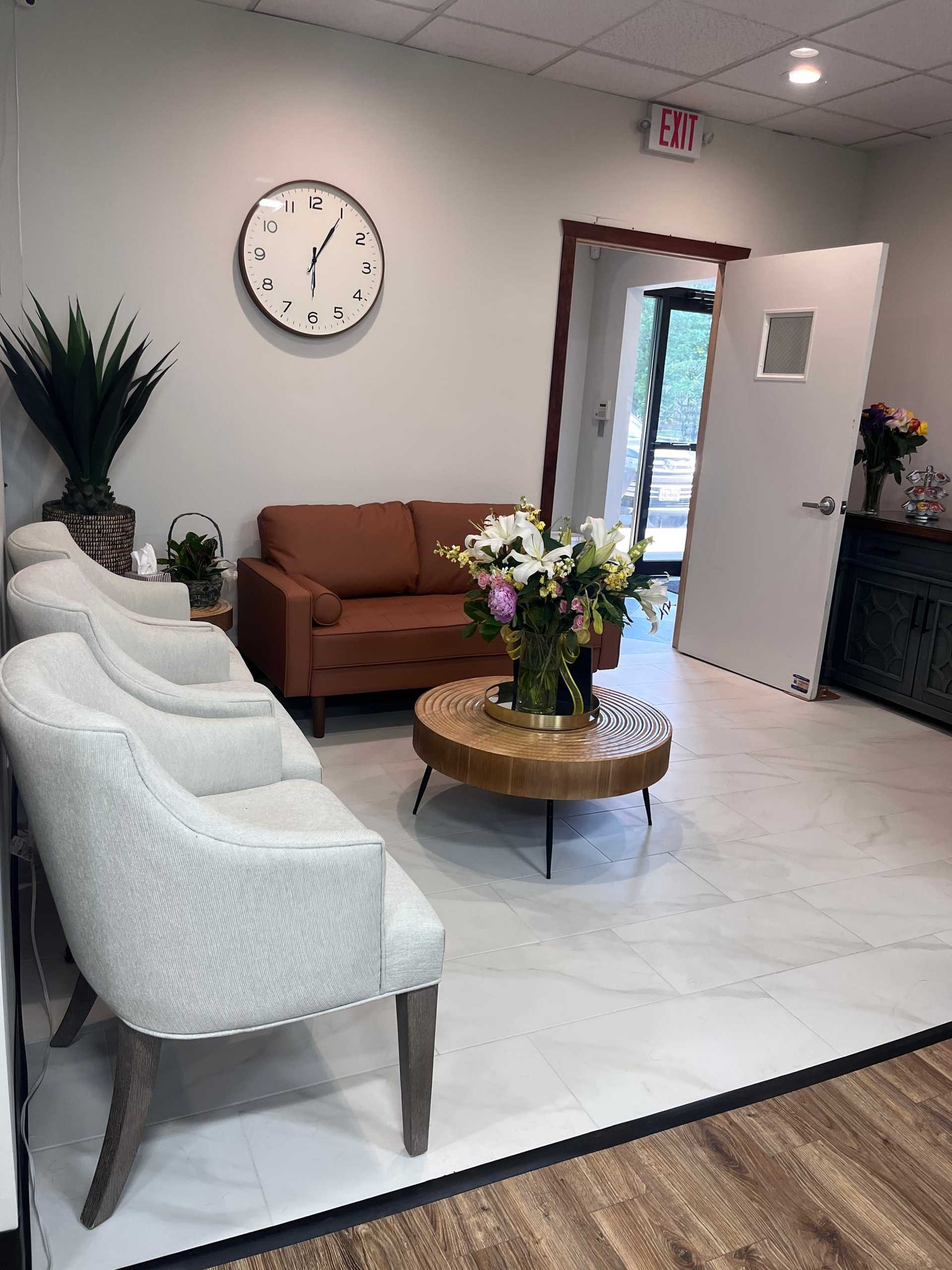 Cozy waiting area with chairs, a clock, and floral arrangement on a round table.