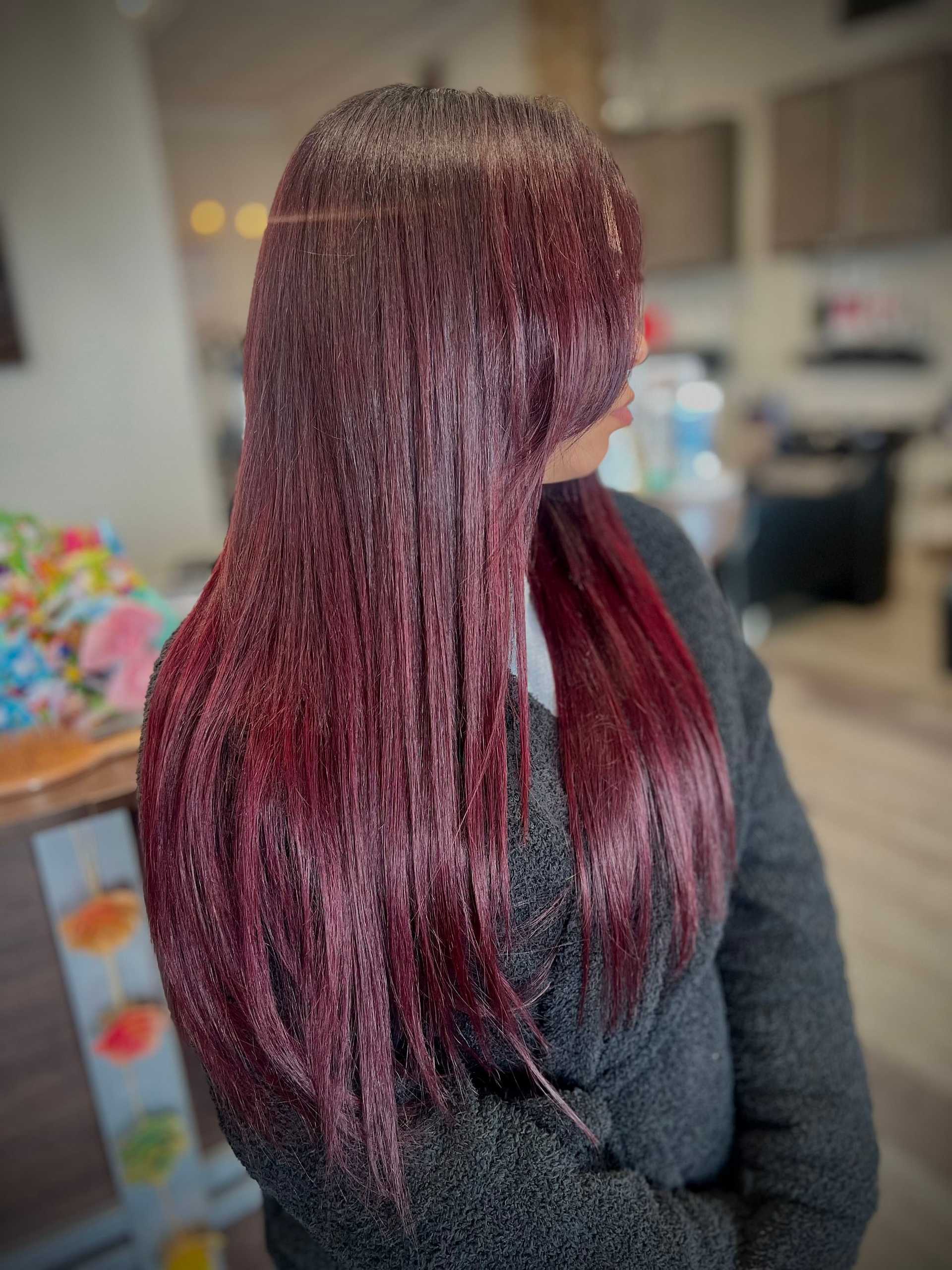 Person with long, straight, burgundy hair in a salon, looking to the side.